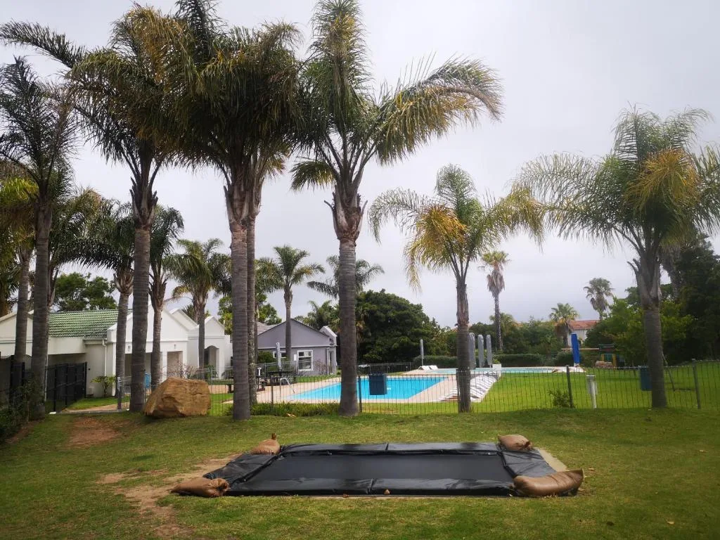 Palm-lined garden with trampoline, pool, and white buildings