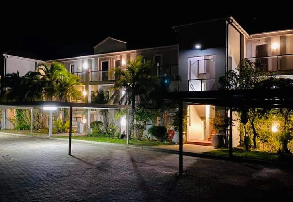 Modern apartment building lit at night with landscaped gardens and patio area
