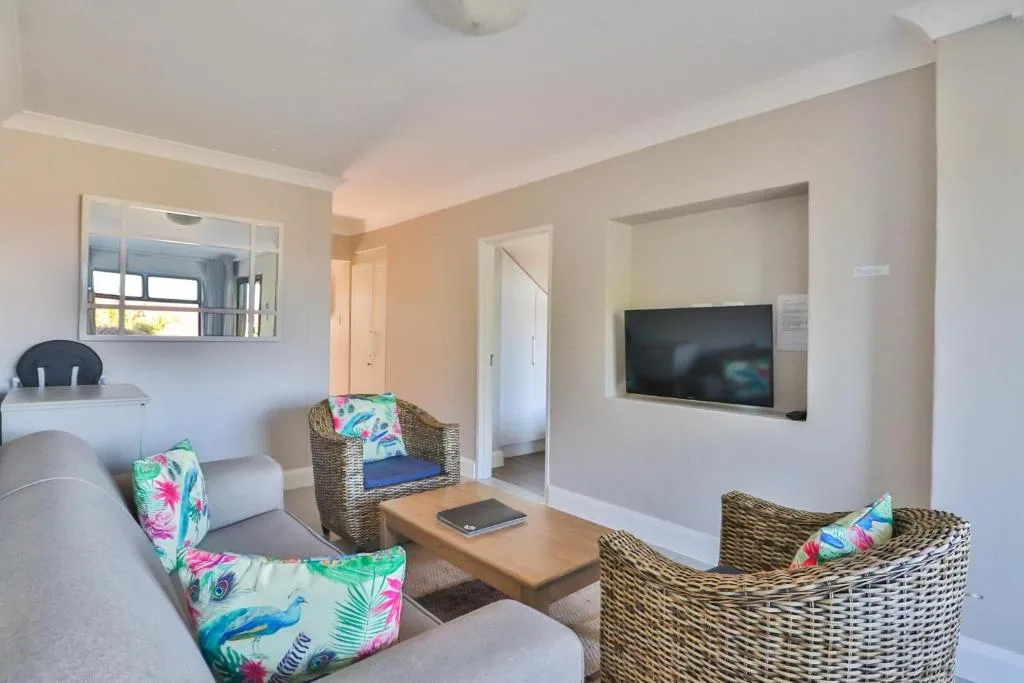 Bright lounge with wicker armchairs, TV, and natural light from windows