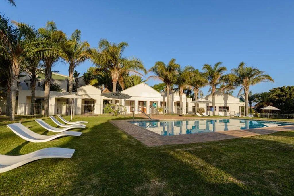 Swimming pool with loungers and manicured gardens, palm trees surrounding white cottages