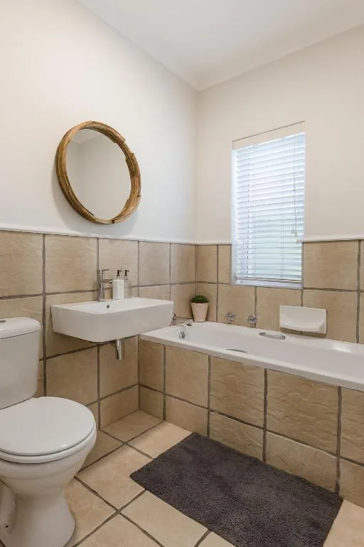 Modern bathroom with dual vanity sinks, toilet, and round mirror
