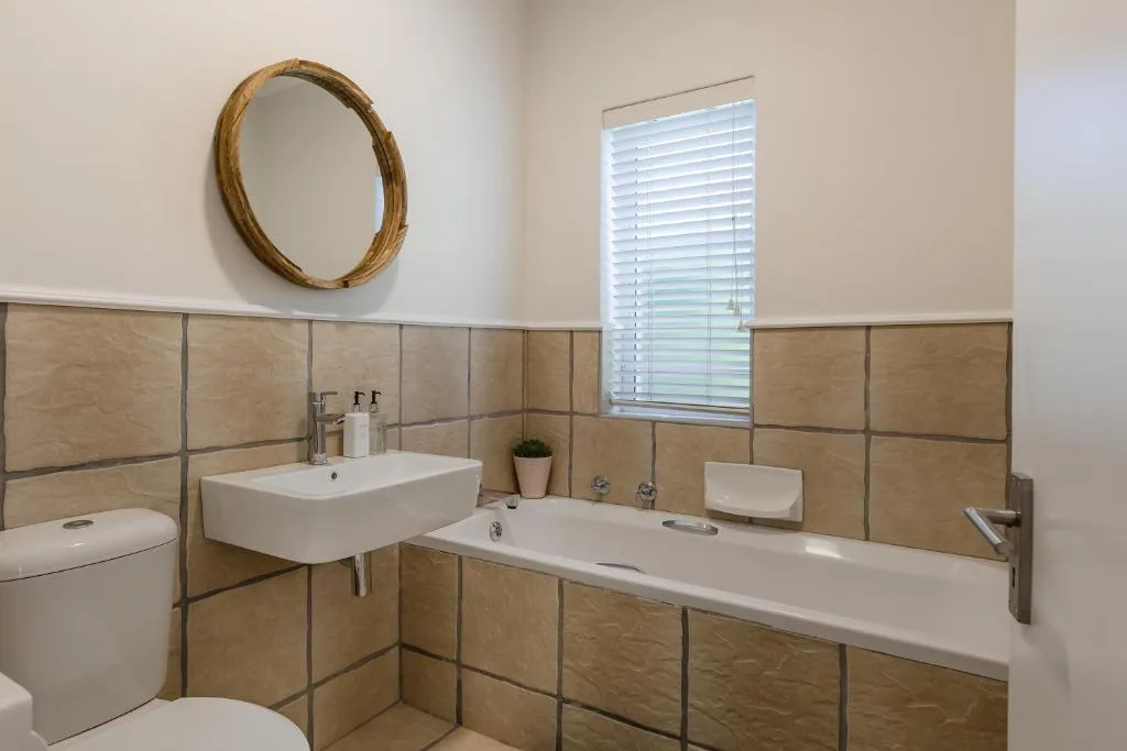 Modern bathroom with dual vanity sinks, toilet, and round mirror