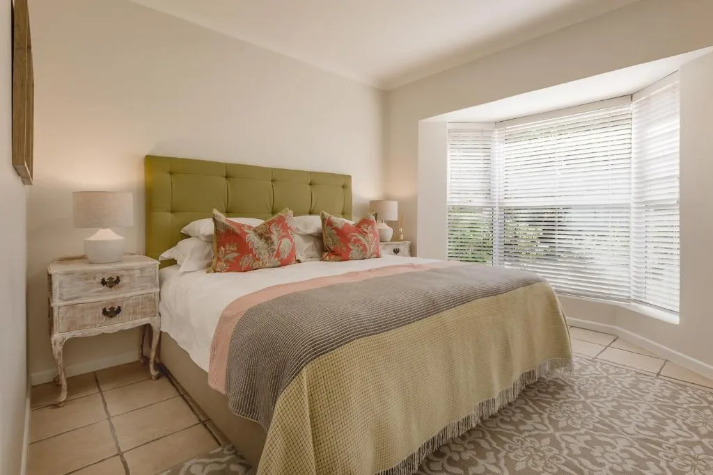 Bright bedroom with olive-green headboard, patterned cushions, and natural light