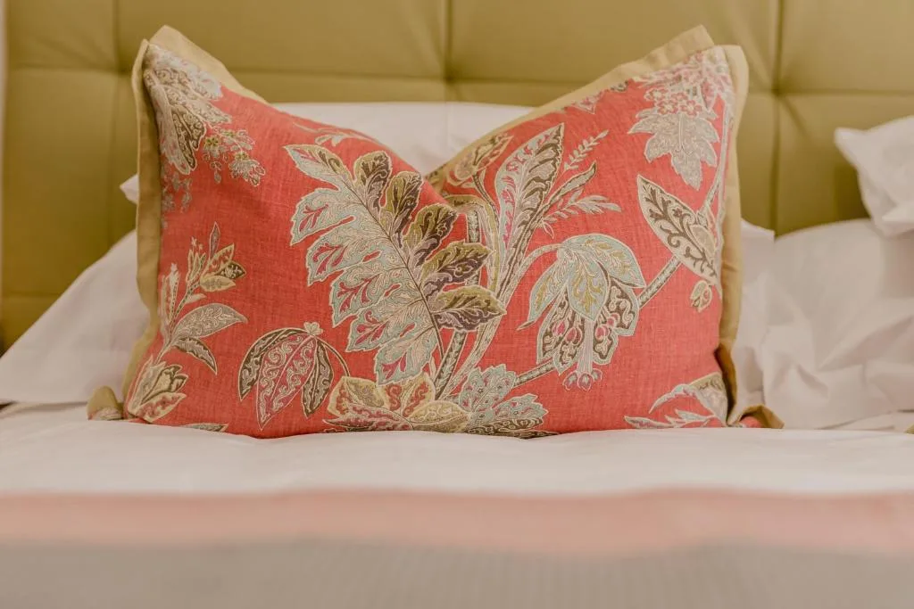 Bed with decorative coral floral pillow and white linens against green headboard