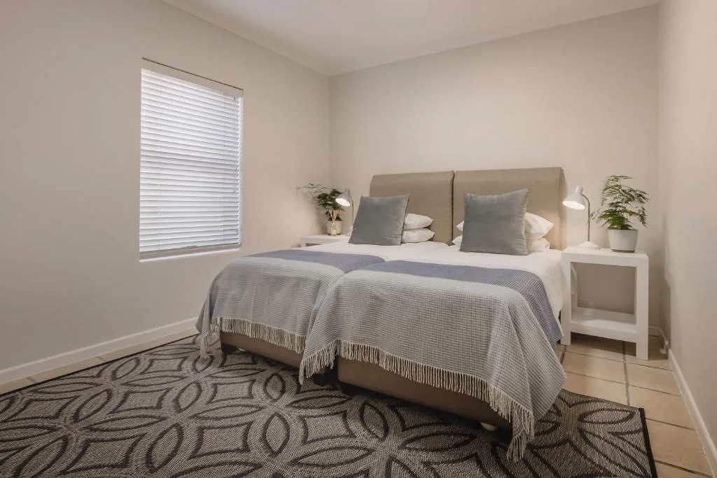 Bright bedroom with neutral bedding, contemporary headboard, and potted plants
