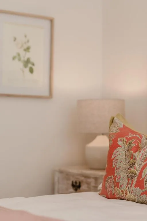 Cozy bedroom corner with decorative red floral pillow and framed botanical art