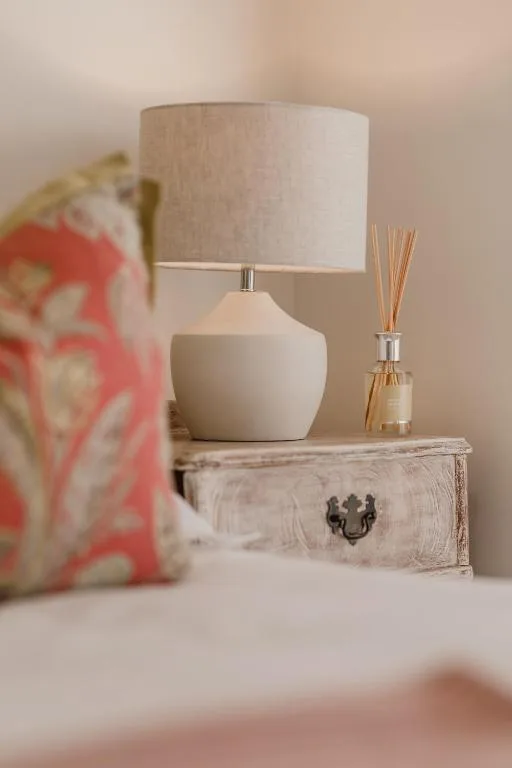 Bedside table with ceramic lamp, reed diffuser, and decorative cushion