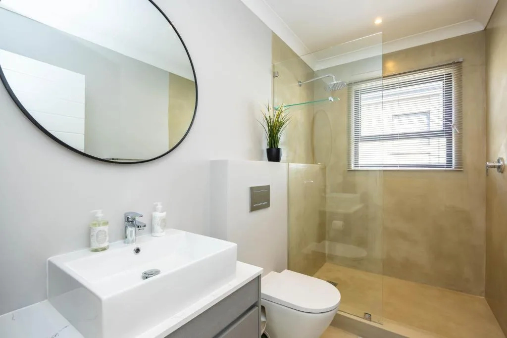 Modern bathroom with white vanity, circular mirror, and glass shower enclosure
