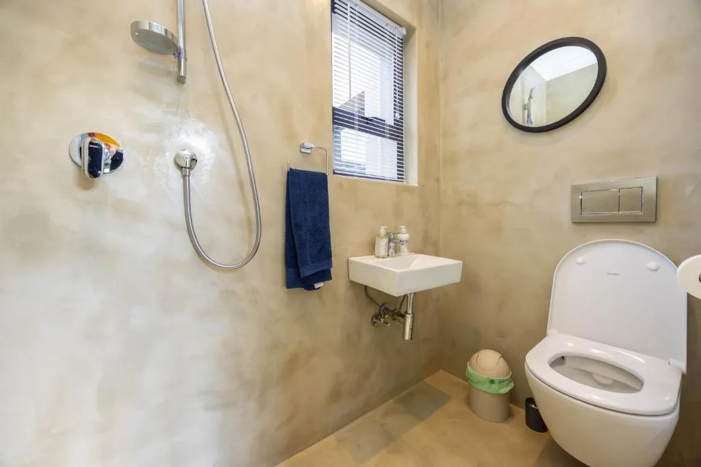 Modern bathroom with shower, wall-mounted sink, toilet, and round mirror