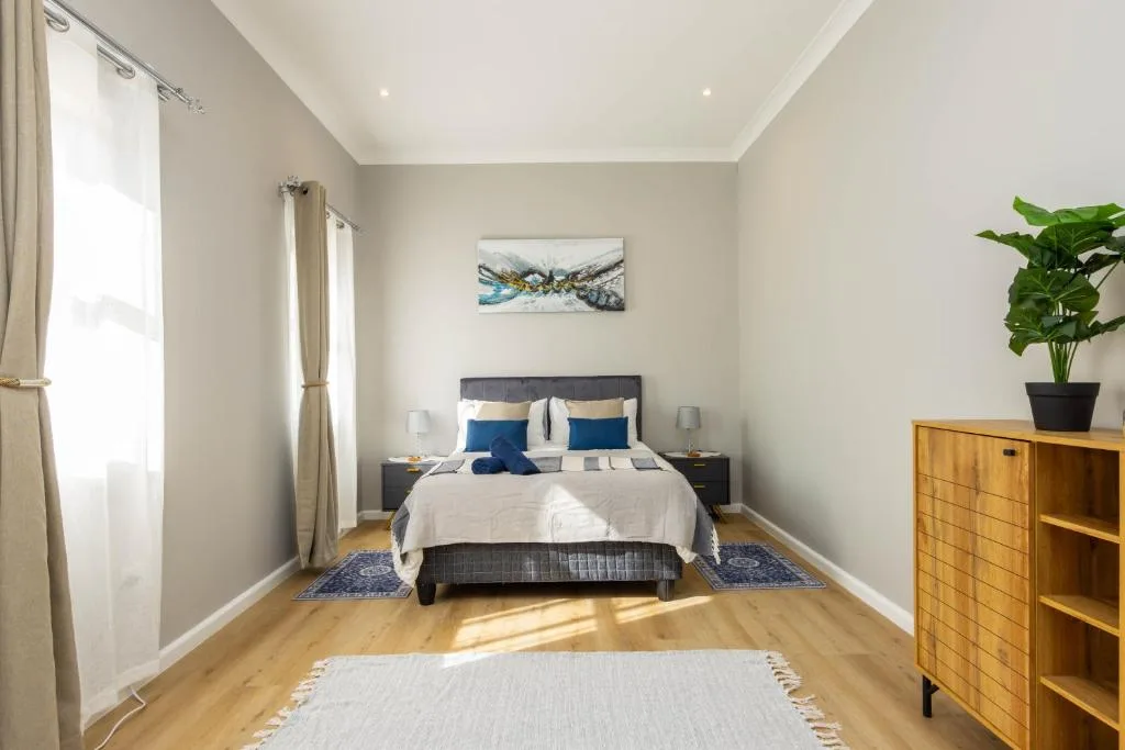 Bright bedroom with queen bed, blue accents, wooden furniture, and natural light