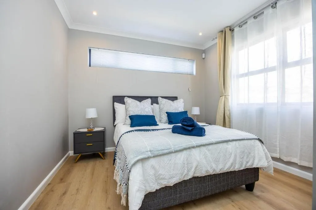 Bright bedroom with made bed, blue accents, bedside table, and large windows