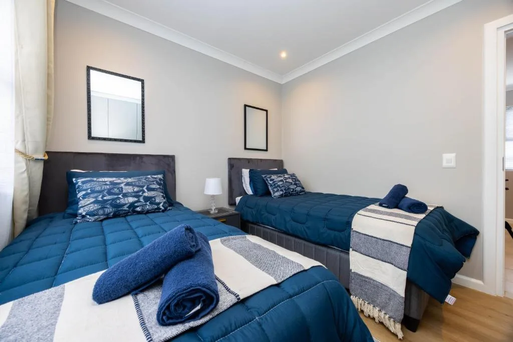 Bright bedroom with two beds, blue bedding, and framed wall art