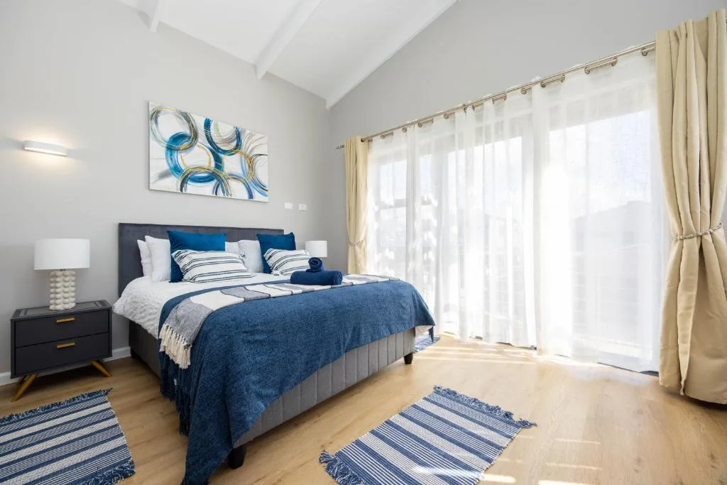 Bright bedroom with blue bedding, modern artwork, and glass doors to deck