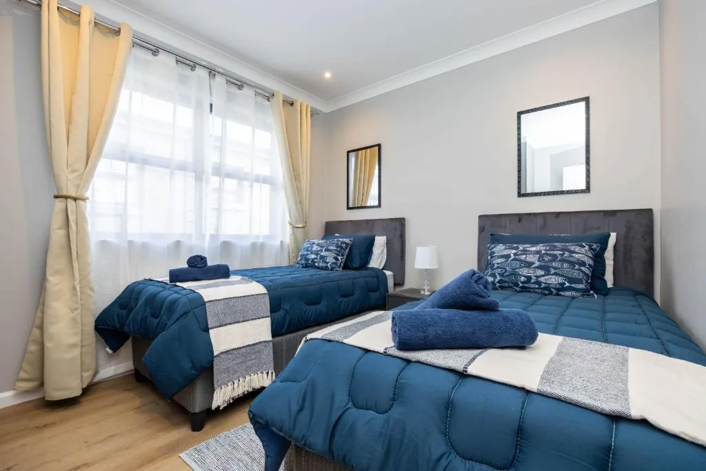 Bright bedroom with three single beds, blue bedding, and large windows with cream curtains