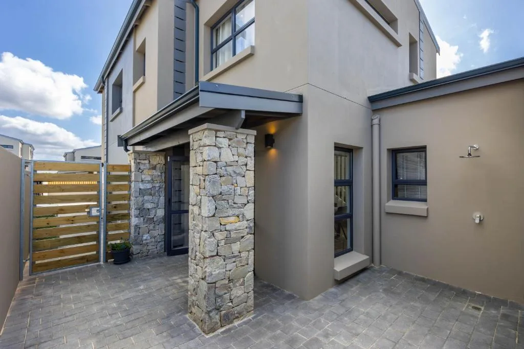 Modern home entrance with stone pillar, wooden gate, and paved courtyard