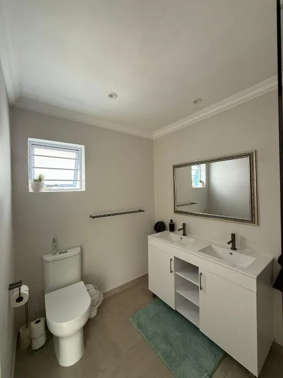 Modern bathroom with white vanity, dual sink, toilet, and framed mirror