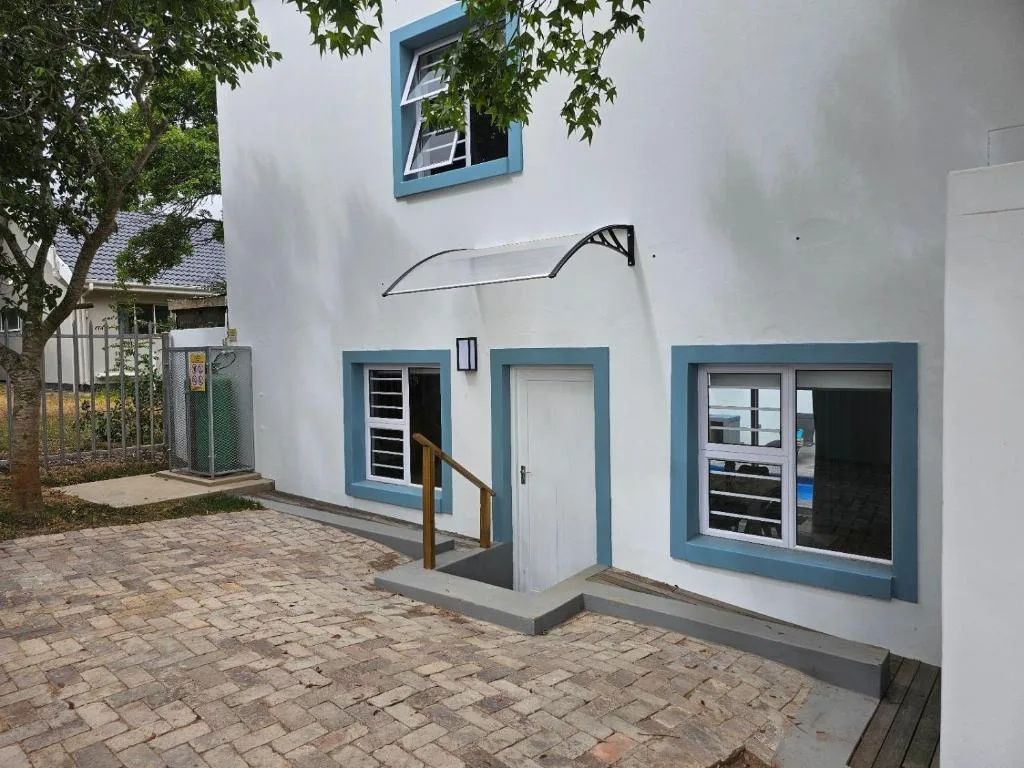 White cottage facade with blue trim and brick paved entrance area