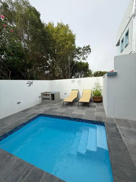 Bright blue swimming pool with loungers and white boundary walls