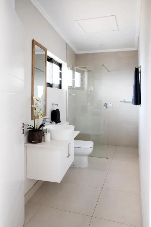 Modern bathroom with white vanity, mirror, toilet, and glass shower enclosure