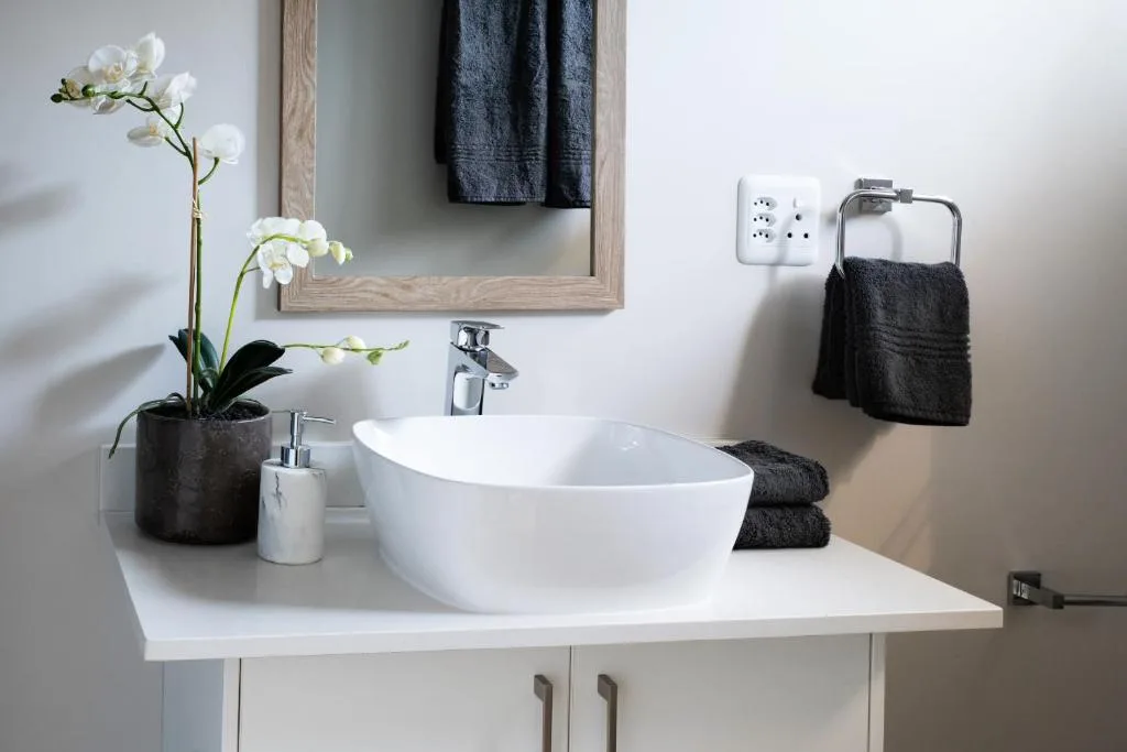 Modern bathroom vanity with white bowl sink, mirror, and black towels