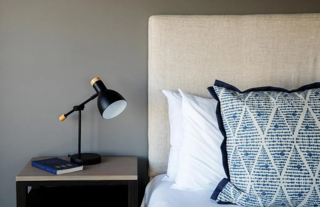 Neutral upholstered bed headboard with blue patterned pillows and reading lamp