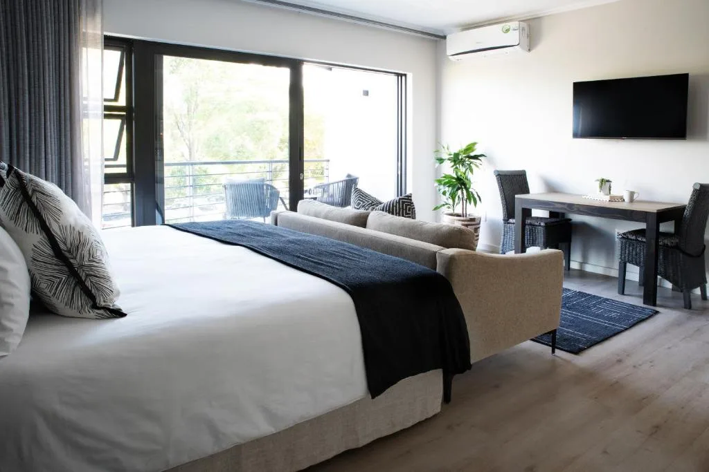 Spacious bedroom with king bed, lounge area, and deck access overlooking greenery