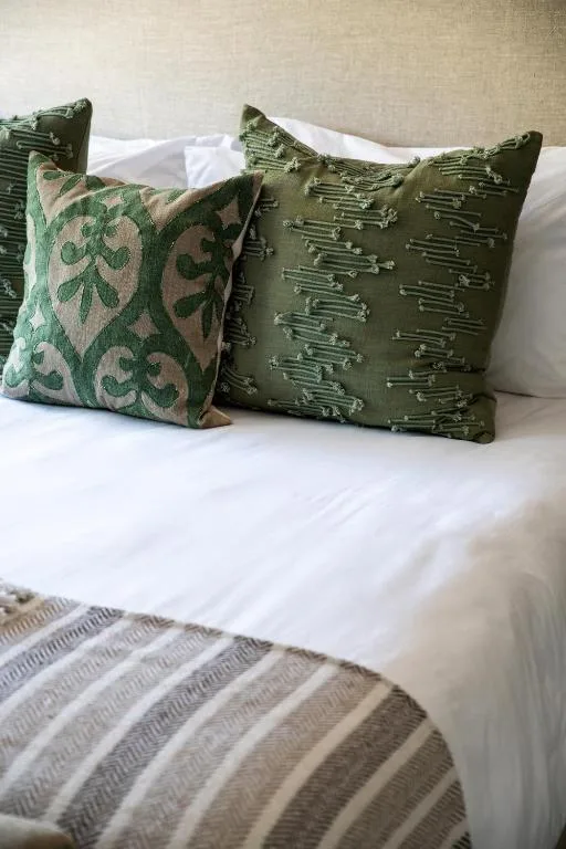 Bed with white linens and patterned green throw pillows