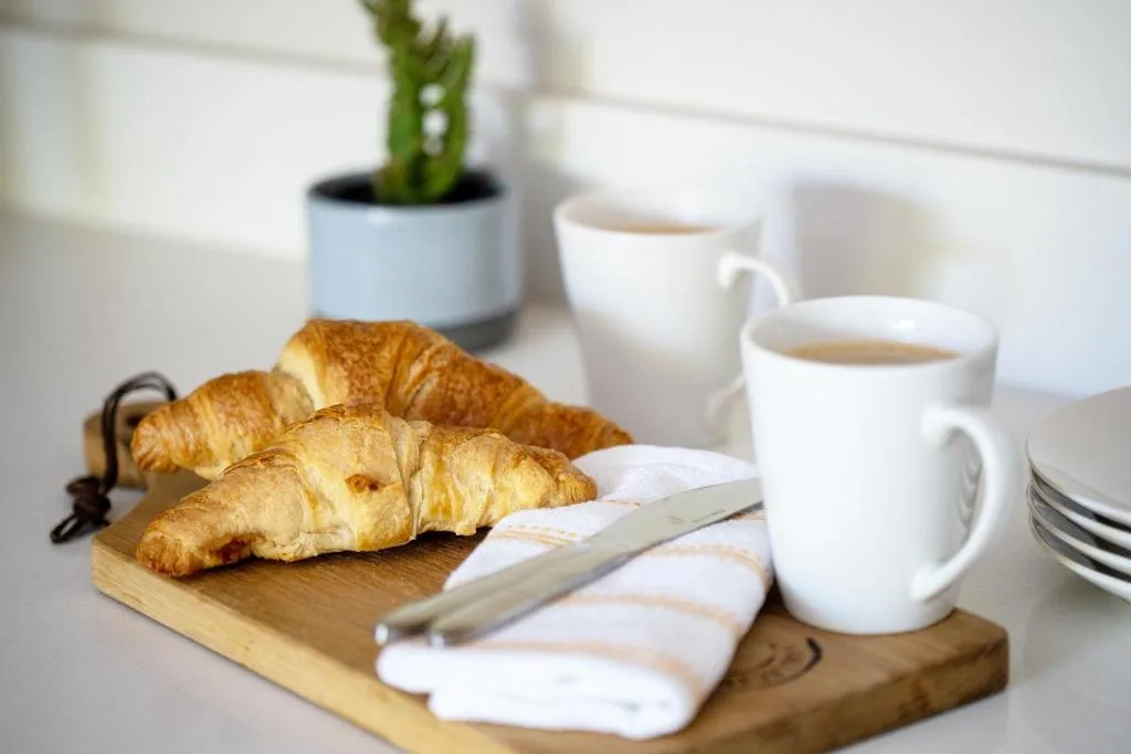 Breakfast setup with croissants, coffee, and fresh pastries on wooden board
