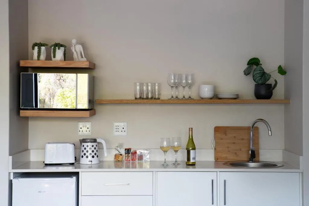 Modern kitchenette with white cabinetry, wooden shelves, and stainless steel sink