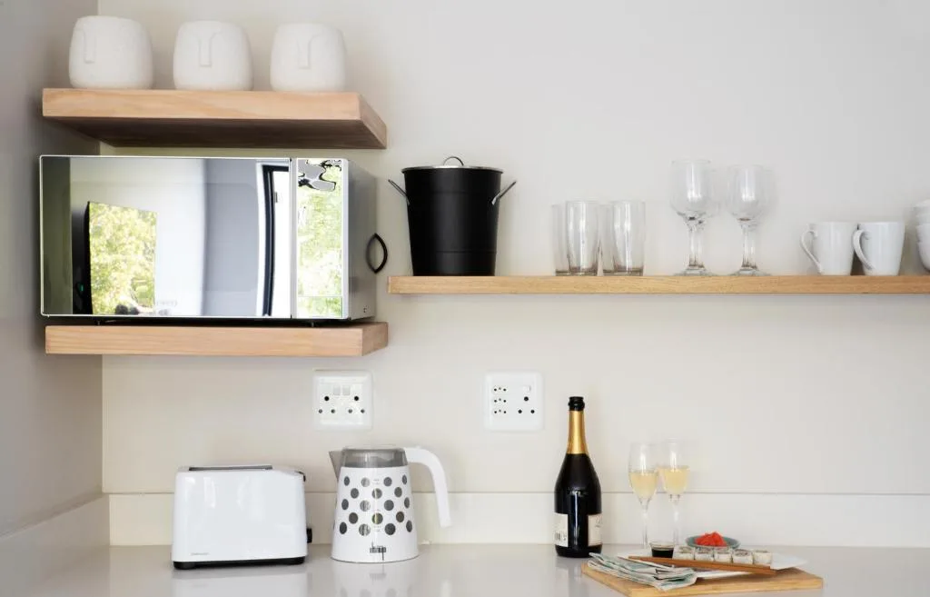Modern kitchen wall with wooden shelves, mirror, appliances, and glassware