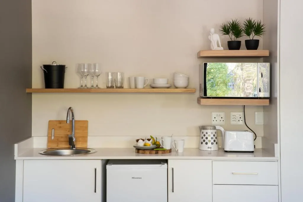 Modern kitchenette with white cabinetry, open shelving, and stainless appliances