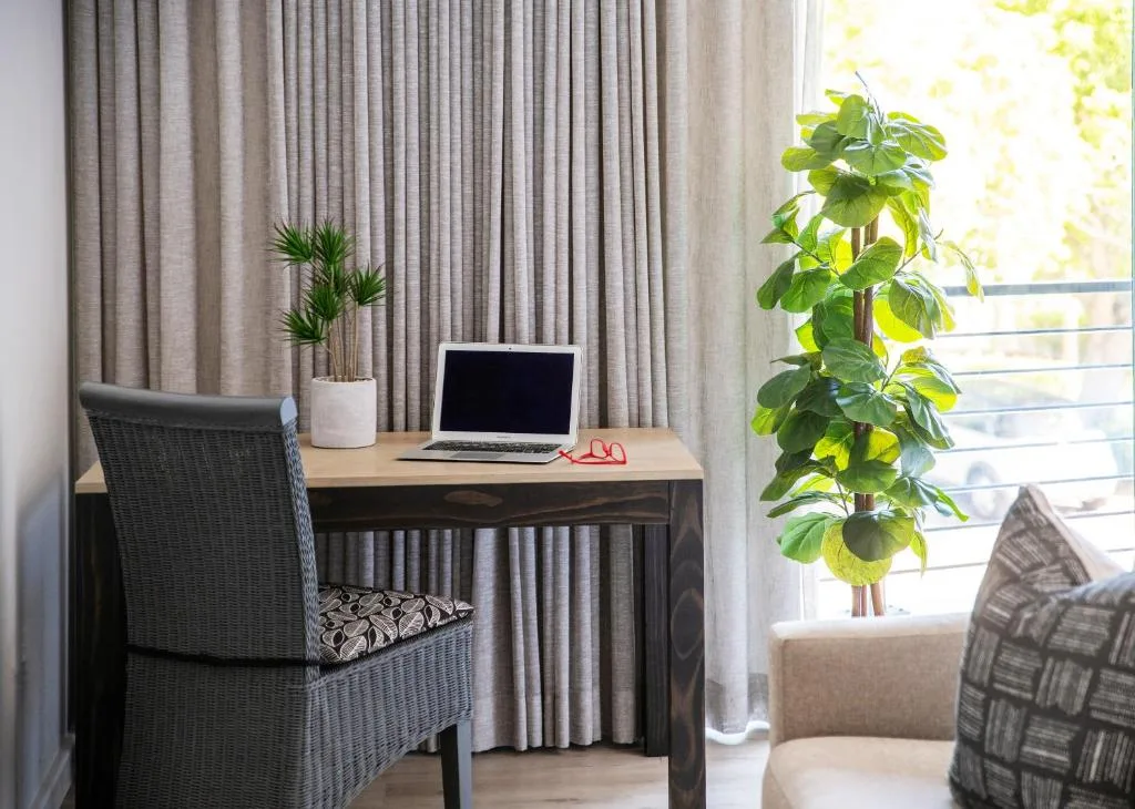Modern lounge workspace with desk, laptop, natural light, and potted plants