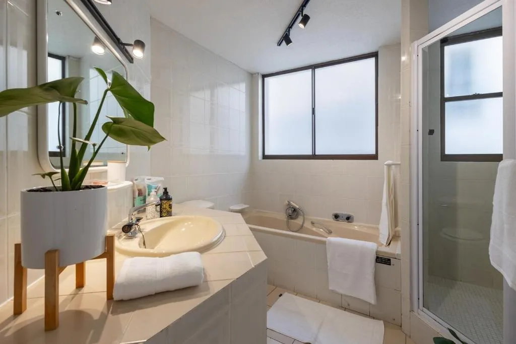 Modern bathroom with dual vanity, bathtub, shower, and potted plant