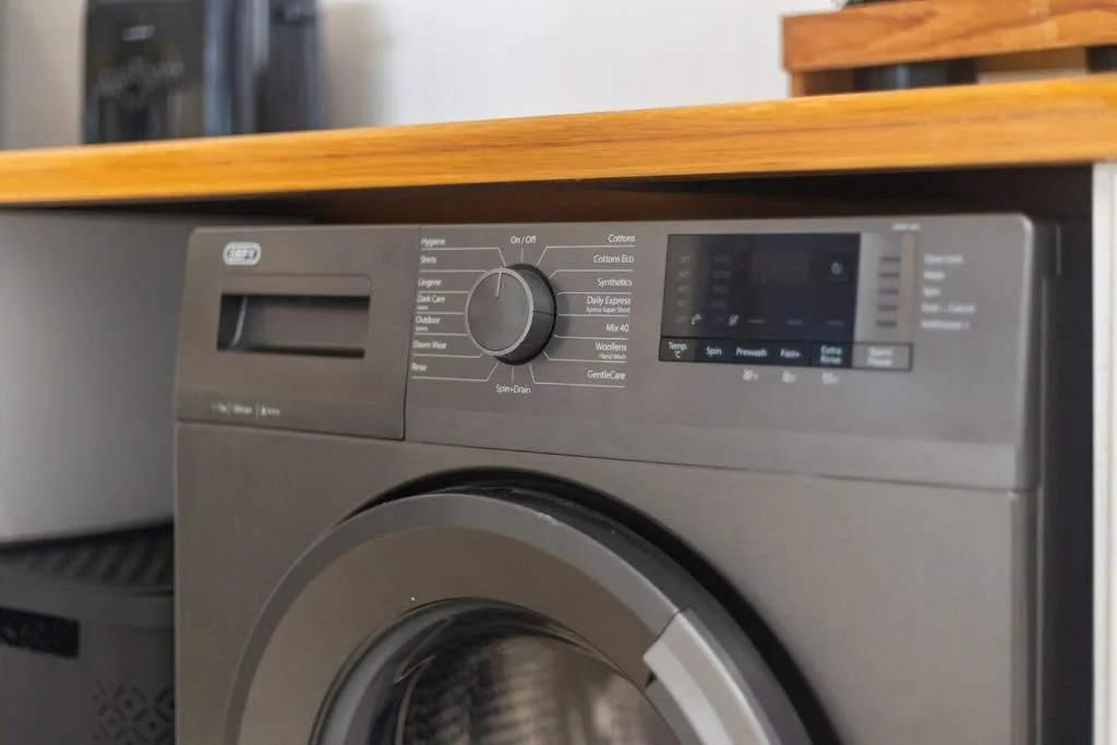 Modern washing machine with digital controls and wooden countertop above