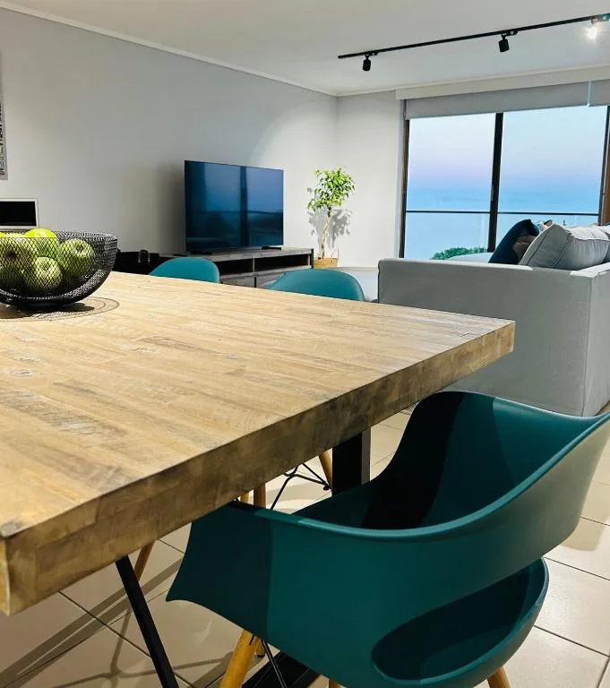 Modern dining area with wooden table, teal chairs, and ocean views
