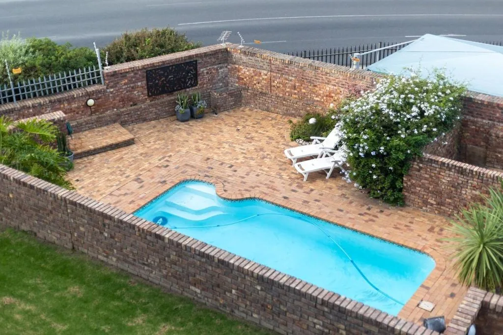 Bright blue swimming pool with loungers and flowering plants on brick patio