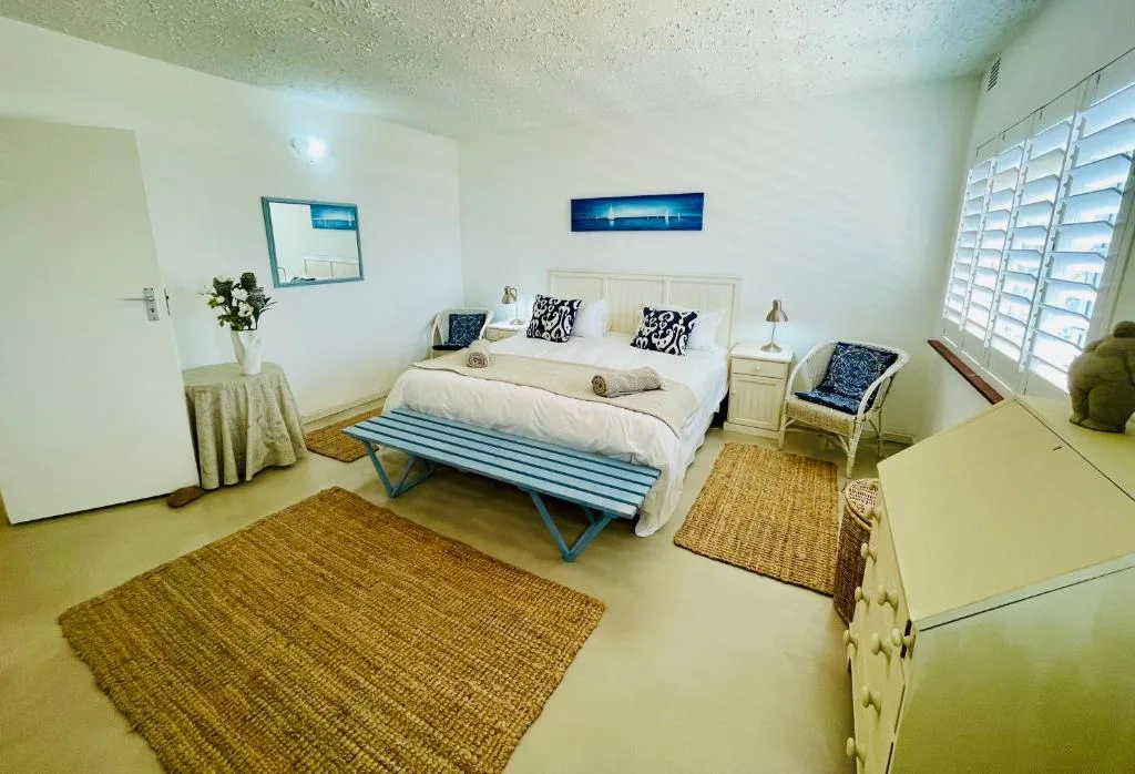 Bright bedroom with queen bed, blue striped bench, nautical decor, and louvered windows
