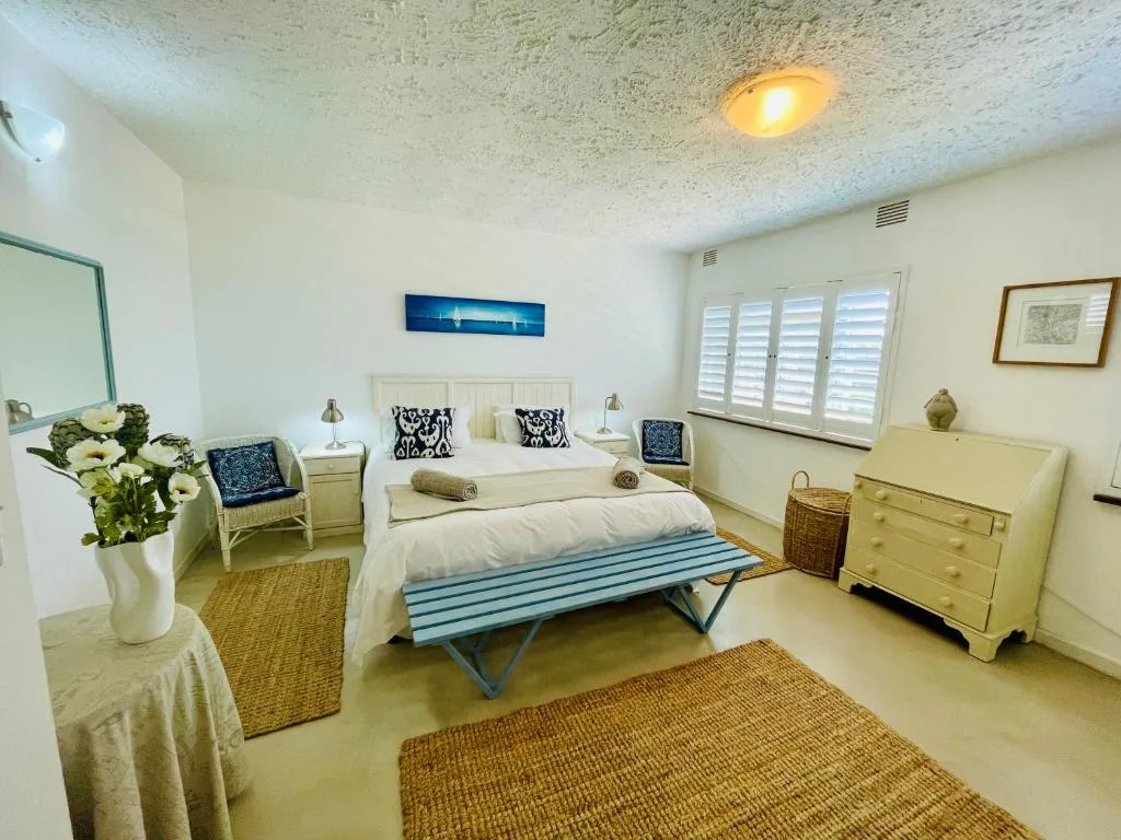 Spacious bedroom with queen bed, coastal decor, shuttered windows, and fresh flowers