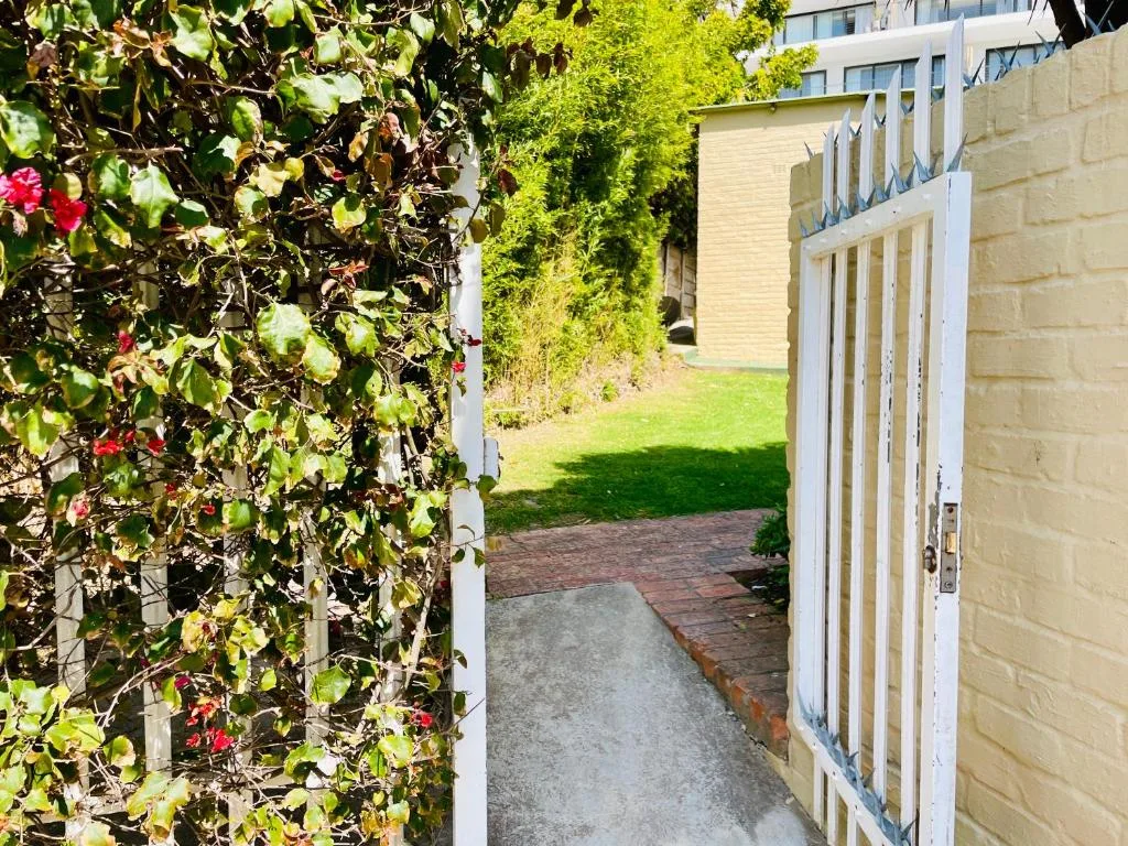 Garden gate entrance with climbing red flowers and lush green lawn beyond