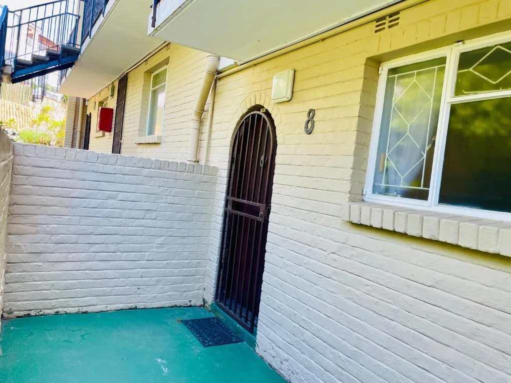 White painted exterior entrance with black arched door and turquoise patio