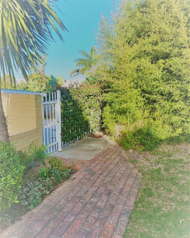 Brick pathway leading to blue gate with white building and lush vegetation