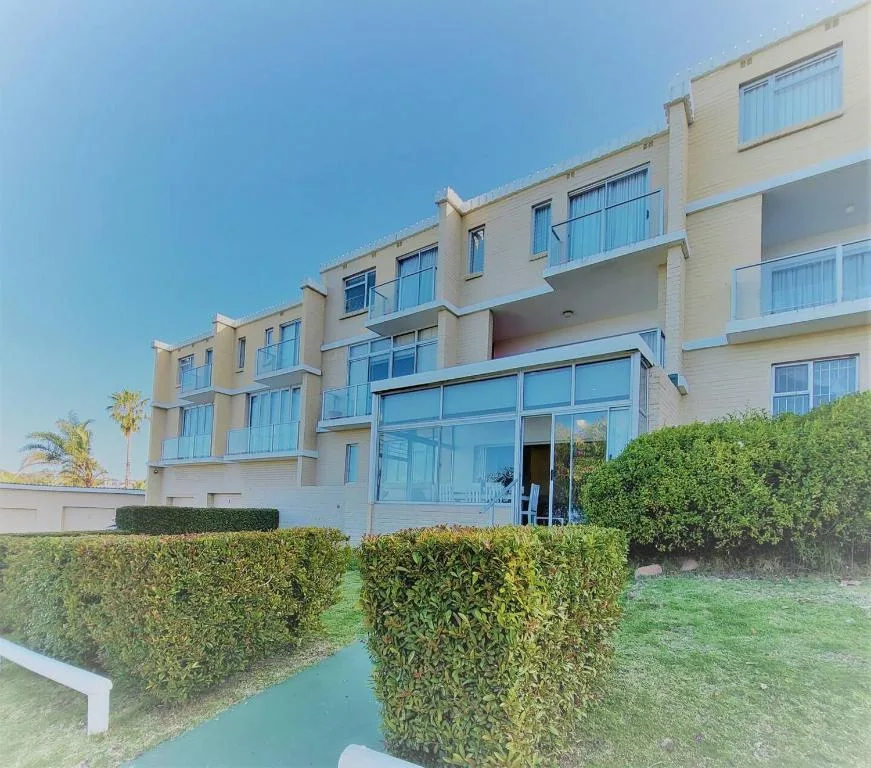Modern cream-colored apartment building with large windows and manicured hedges.