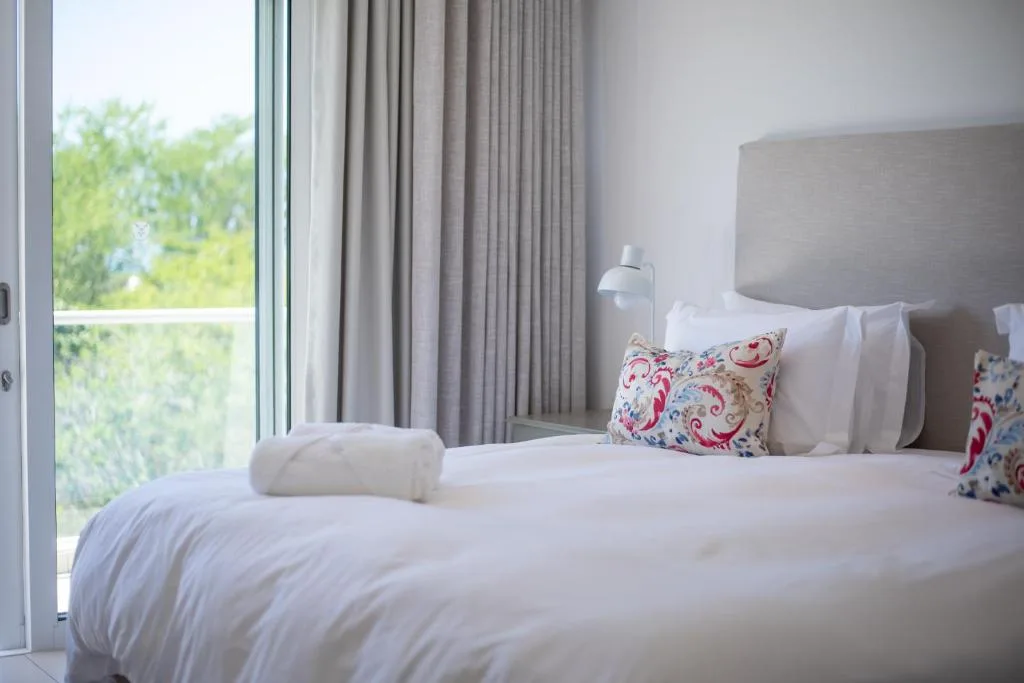 Bright bedroom with twin beds, colorful pillows, and garden views through large windows