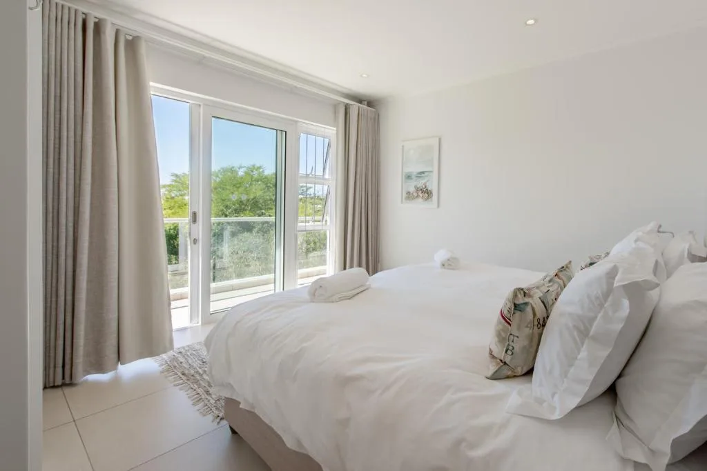 Bright bedroom with white bedding and garden views through glass doors