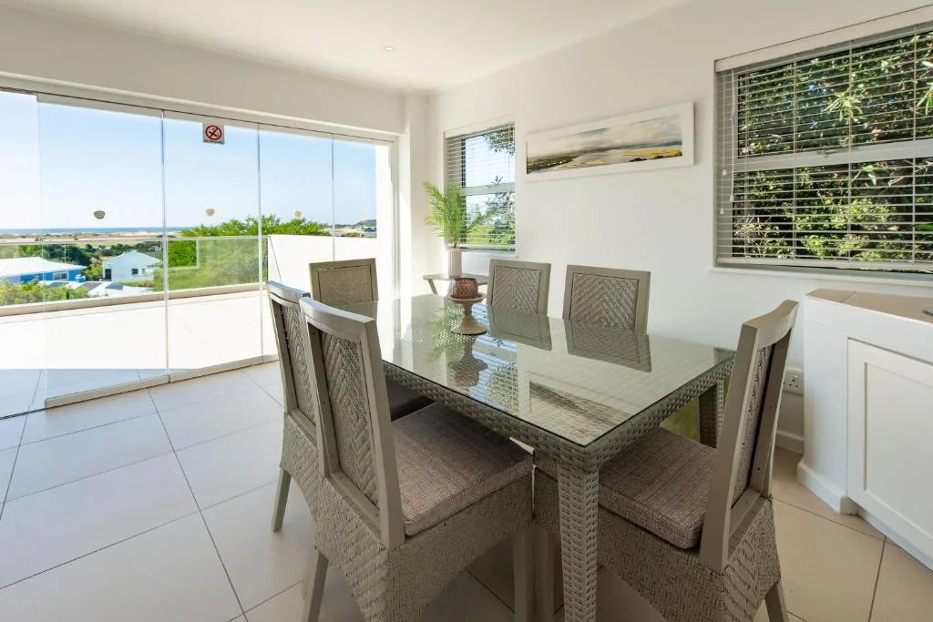 Modern dining table with six woven chairs overlooking coastal views through glass doors