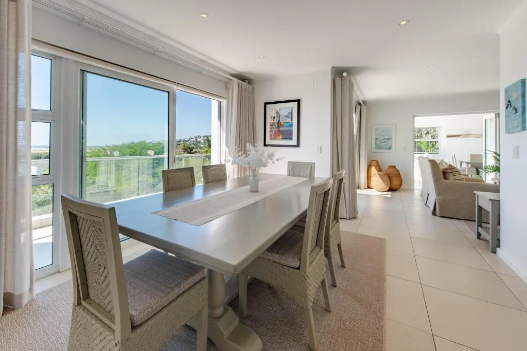 Bright dining room with white table, upholstered chairs, panoramic windows overlooking garden