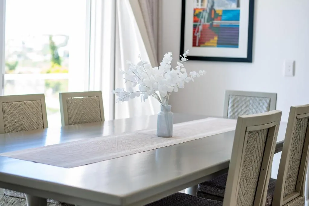 Bright dining area with white table, woven chairs, fresh flowers, and artwork
