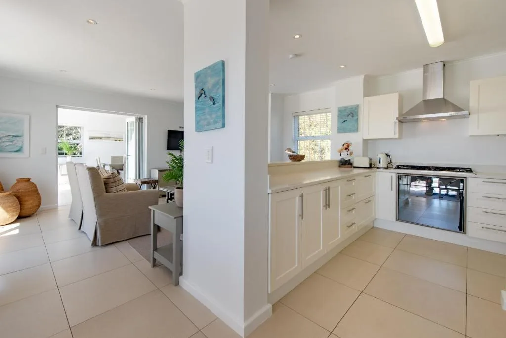 Modern open-plan kitchen with cream cabinetry, stainless steel appliances, and adjacent lounge
