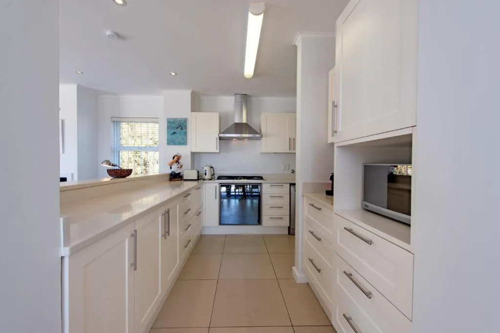 Modern white kitchen with cream countertops, stainless steel appliances, and natural light