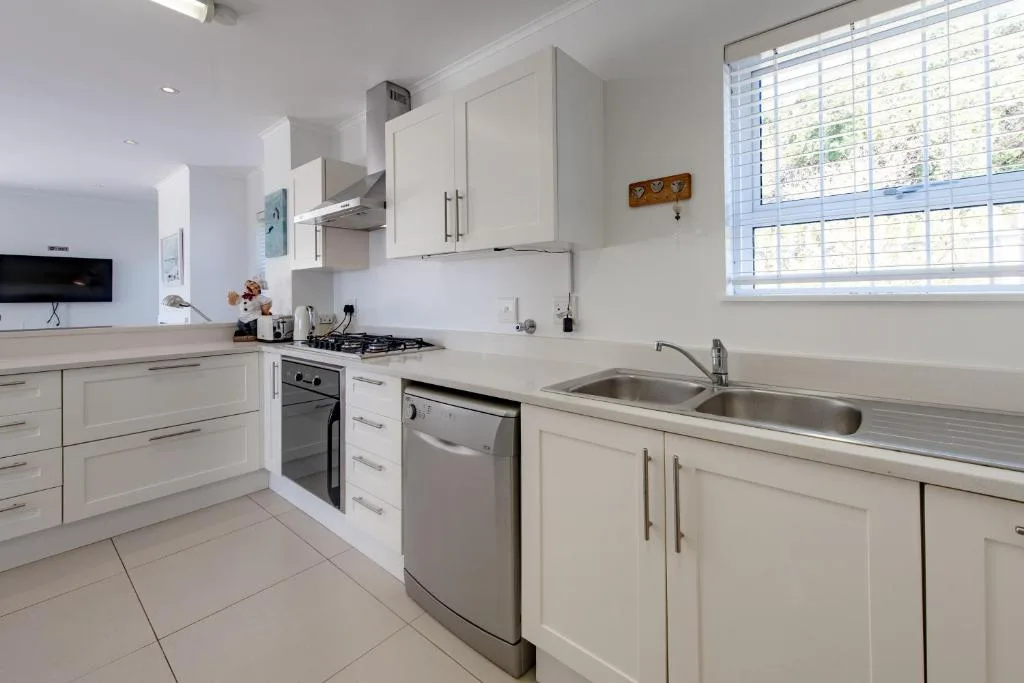 Modern white kitchen with gas stove, dishwasher, double sink, and natural light